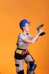 Woman construction worker on ladder drilling wall with cordless drill indoors. Professional female...