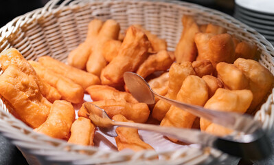 Homemade deep-fried traditional Thai dough sticks with Tong, served in a basket at the hotel’s buffet, with selective focus. Golden brown Asian appetizer, famous street food in Thailand and Asia.