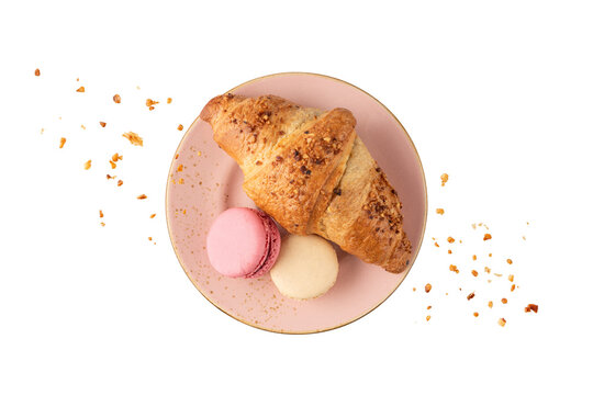 Fresh baked nut croissant and french cookies macarons macaroons with crumbs on vintage pink plate isolated on white background.