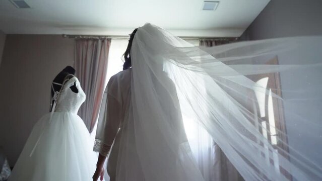 Bride in white boudoir dress goes to her dress. Veil in slow motion.
