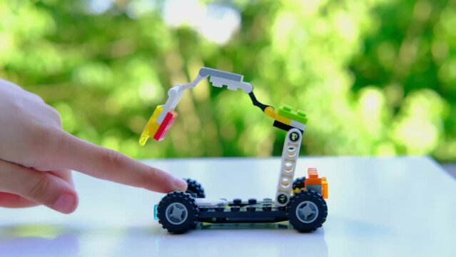 child's fingers move transformer car with manipulator, assembled from blocks parts, beautiful green background of trees, concept development, creativity, children's entertainment, Frankfurt - June 2022