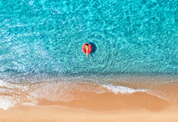 Obraz premium Beautiful seascape with woman with red swim ring in blue sea at sunset in summer. Aewrial view. Tropical scenery with girl, clear water, waves, sandy beach. Top view. Vacation. Sardinia island, Italy 