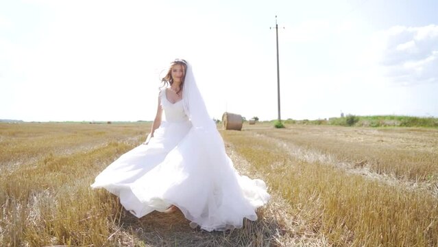 Happy young woman in white dress running on the field with wheat. Slow motion