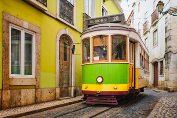 Famous vintage yellow tram 28 in the narrow streets of Alfama district in Lisbon, Portugal - symbol of Lisbon, famous popular travel destination and tourist attraction - obrazy, fototapety, plakaty
