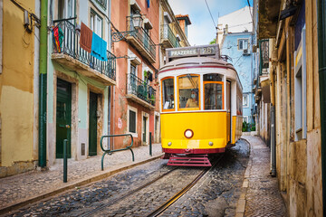 Naklejka na ściany i meble Famous vintage yellow tram 28 in the narrow streets of Alfama district in Lisbon, Portugal - symbol of Lisbon, famous popular travel destination and tourist attraction