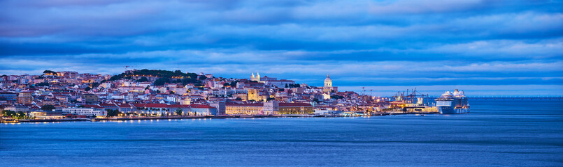 View of Lisbon over Tagus river with passing ferry boat from Almada with moored cruise liner in evening twilight. Lisbon, Portugal