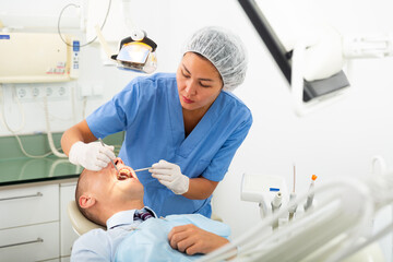 Woman dentist and businessman patient sitting in medical chair during checkup at dental clinic office