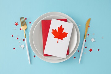 1st of July Victoria day table decoration idea. Top view photo of plate with card and red maple leaf, cutlery and white red stars confetti on light blue backdrop
