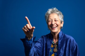 Conceptual portrait photography of a joyful mature woman making a i'm thinking gesture with the finger on the temple against a royal blue background. With generative AI technology