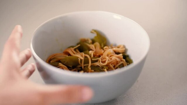 Vista a&eacute;rea de un bol con noodles y pimientos verdes. Moviendo los fideos con un tenedor. Comida asi&aacute;tica.
