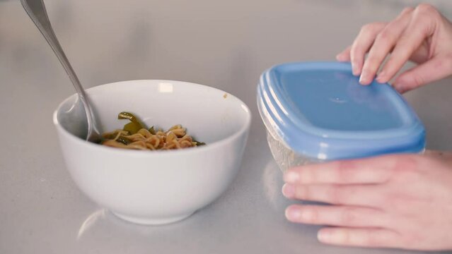 Detalle de una mujer moviendo con un tenedor los noodles dentro de un bol sobre la encimera de la cocina junto a un tupperware de pl&aacute;stico que cierra despu&eacute;s