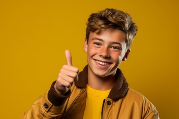 Headshot portrait photography of a grinning boy in his 20s showing a thumb up against a mustard yellow background. With generative AI technology
