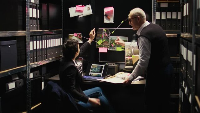 Law agents team inspecting clues and evidence authenticity, analyzing details placed on wall board. Criminologist and police officer conducting private investigation in incident room.
