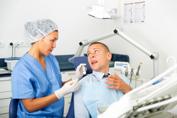 Qualified woman dentist working in the clinic examines a man patient sitting in a dental chair
