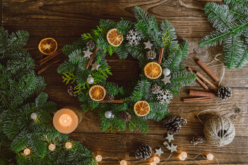 Christmas wreath made of natural branches, orange slices and New Year's decor on a wooden background. View from above.