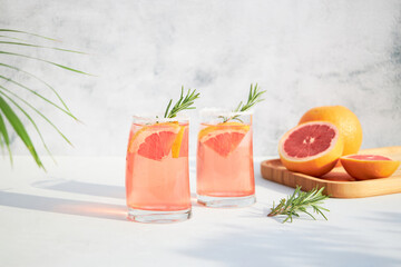 Two glasses with a fresh, cold summer cocktail of grapefruit and ice, garnished with a sprig of...