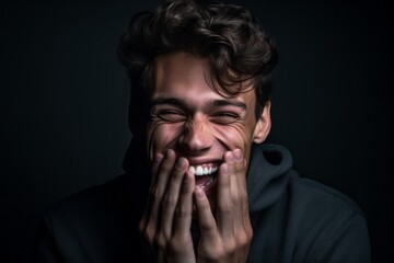 Close-up portrait photography of a glad boy in his 20s placing the hand over the mouth in a laughter gesture against a matte black background. With generative AI technology