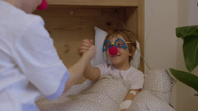 Medical sister with a red nose plays with a boy in his hospital ward