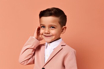 Medium shot portrait photography of a satisfied kid male making a i'm listening gesture with the hand on the ear against a salmon pink background. With generative AI technology
