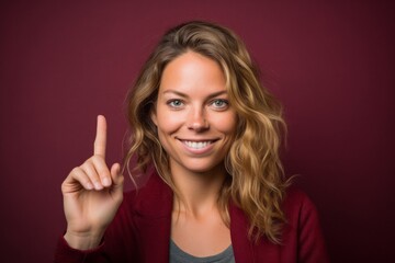 Headshot portrait photography of a glad girl in her 30s making a peace gesture with two fingers against a rich maroon background. With generative AI technology