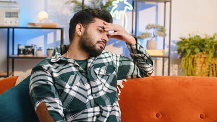 Sad lonely man sitting at home room looks pensive thinks over life concerns or unrequited love...