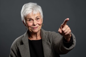 Environmental portrait photography of a satisfied mature woman raising a finger as if having an idea against a cool gray background. With generative AI technology