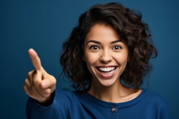 Close-up portrait photography of a happy girl in her 30s pointing up against a sapphire blue background. With generative AI technology