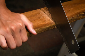 Person cutting wood with handsaw (detail)