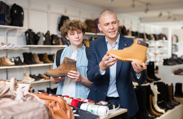 Father and son choose and buy fashionable brown winter boots in a shoe store