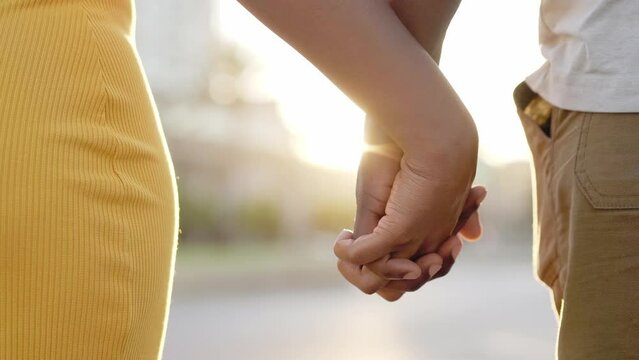 Close up of intertwined hands with sunset sunlight in background. Young African couple holding hands on a sunny summer day. People enjoying romantic moments.