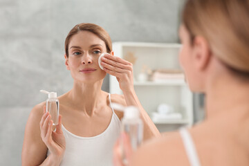 Obraz na płótnie Canvas Beautiful woman removing makeup with cotton pad near mirror indoors