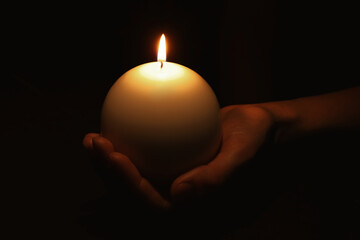 Woman holding burning candle in hand on black background, closeup