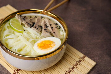 Bowl of delicious rice noodle soup with meat and egg on brown table, closeup. Space for text