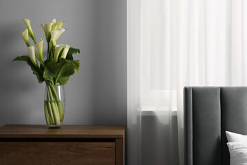 Beautiful calla lily flowers in vase on wooden bedside table