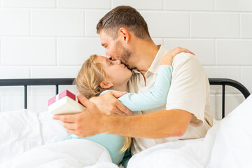 Fototapeta premium Father wake up a sleeping child daughter on the bed in bedroom in sunny morning. Happy family start a new day together with freshness. Little girl waking up with smiling.