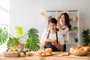 Asian man and woman preparing food and bread to make a healthy breakfast. Enjoying cooking with joy, a charming wife and cheerful husband are preparing delightful meals with fresh ingredients.