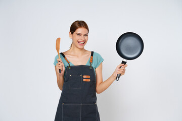 Young woman wearing kitchen apron cooking and holding pan and spatula isolated on white background.