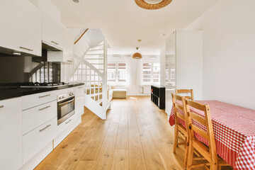 a kitchen and dining area in a house with white walls, wood floors and an open staircase leading up to the second floor