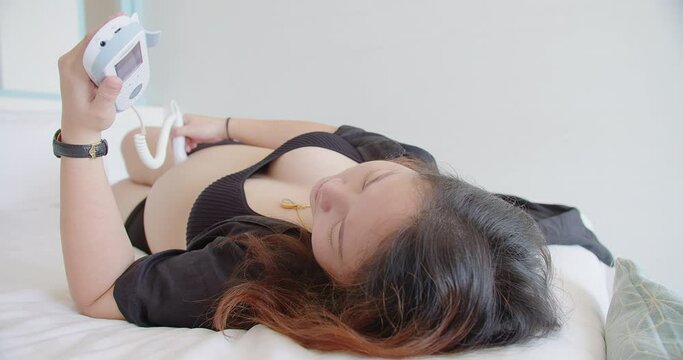 Beautiful happiness pregnant woman does ultrasound probe moving over pregnant belly on her self, using fetal doppler device for listening hear baby heartbeat device, motherhood health care baby