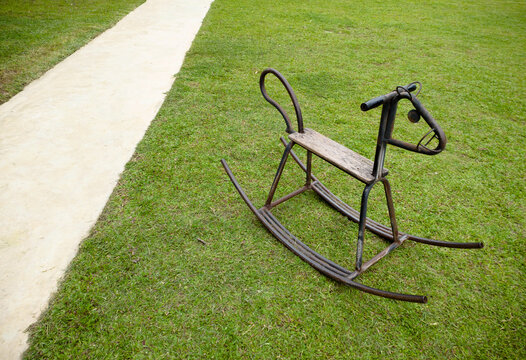 An iron rocking horse sits on a path in the grass.