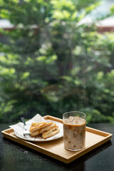 Iced coffee in glass on wooden table and green garden background.