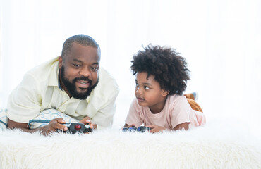 African father and child son playing online video games, using joysticks or game console, having fun at home, lying on bed and enjoying time together. White background