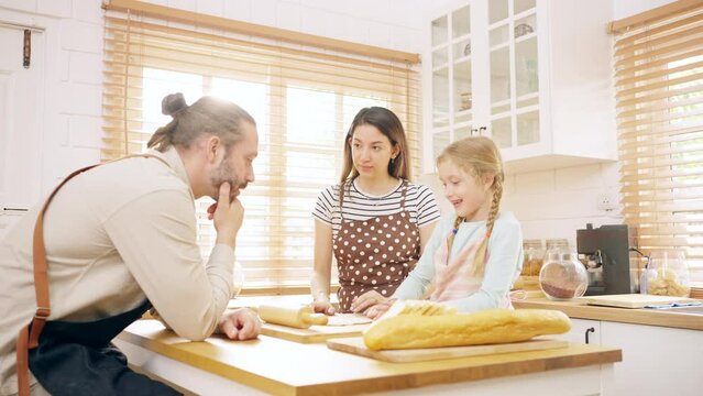 Caucasian father and mother teach little daughter kneading dough in the kitchen at home. Parents and child girl kid enjoy indoors activity lifestyle cooking meal together. Family relationship concept.