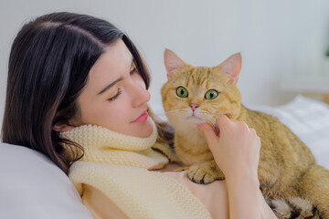  beautiful young asian woman cherishes a playful moment with her adorable cat on a cozy bed, bathed in bright morning light filtering through white window curtains