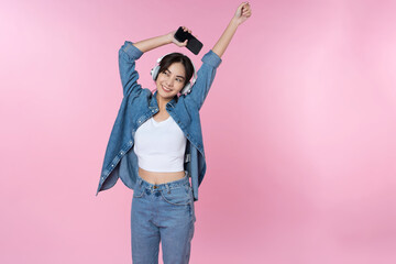 Fototapeta premium Young Asian woman wearing headphones dancing and listening to music from smartphone shoot in isolated on pink background