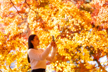 Happy Asian woman travel Japan on autumn holiday vacation. Attractive girl using mobile phone taking selfie during travel Lake Kawaguchi and Mt Fuji with looking beautiful red maple tree leaf falling.
