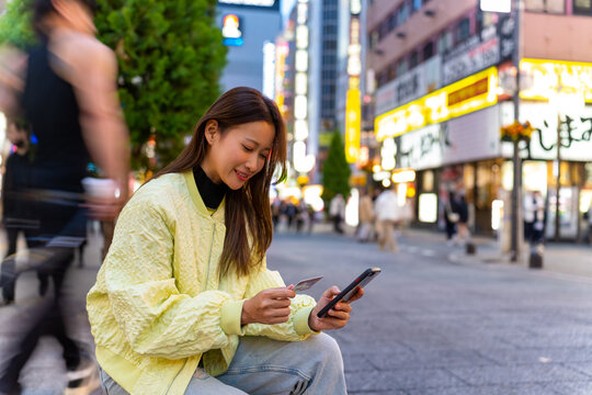 Asian woman using mobile phone with credit card booking hotel or online shopping during travel in Japan. Attractive girl enjoy outdoor lifestyle travel and shopping in the city on holiday vacation.