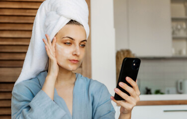 Woman in a blue bathrobe and with a towel on her head sits on th