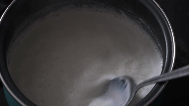 hand stirring with a metal spoon, food from a pot in the kitchen, preparing a recipe close-up
