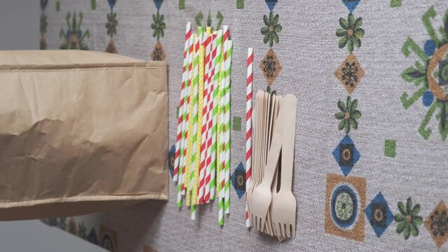 woman's hand takes cutlery and paper plates, cups, cardboard and wooden forks from a bag and leaves it on the table, sustainable, biodegradable and ecological cutlery

